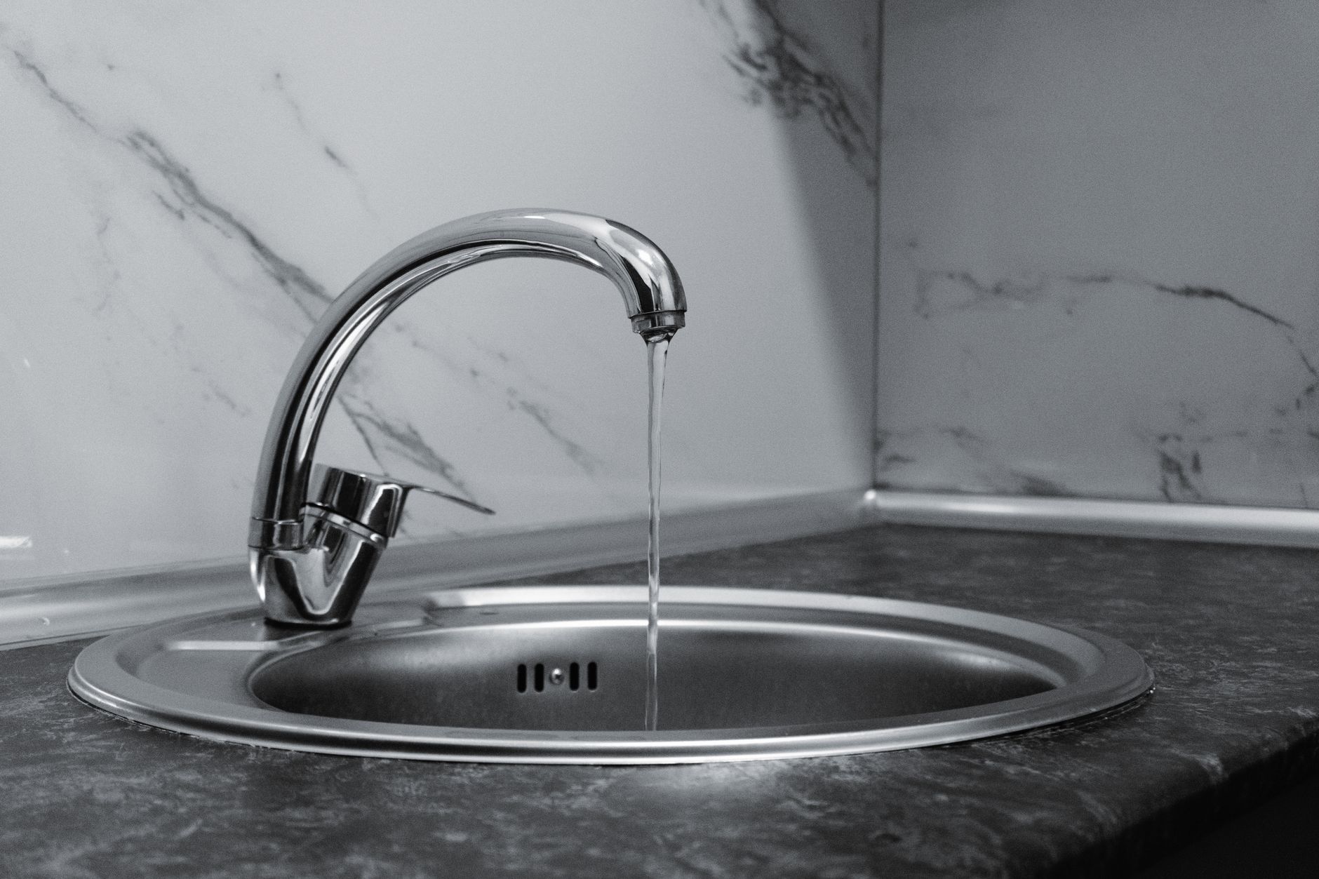 Chrome faucet with running water in a modern kitchen with marble countertop in Round Rock, TX